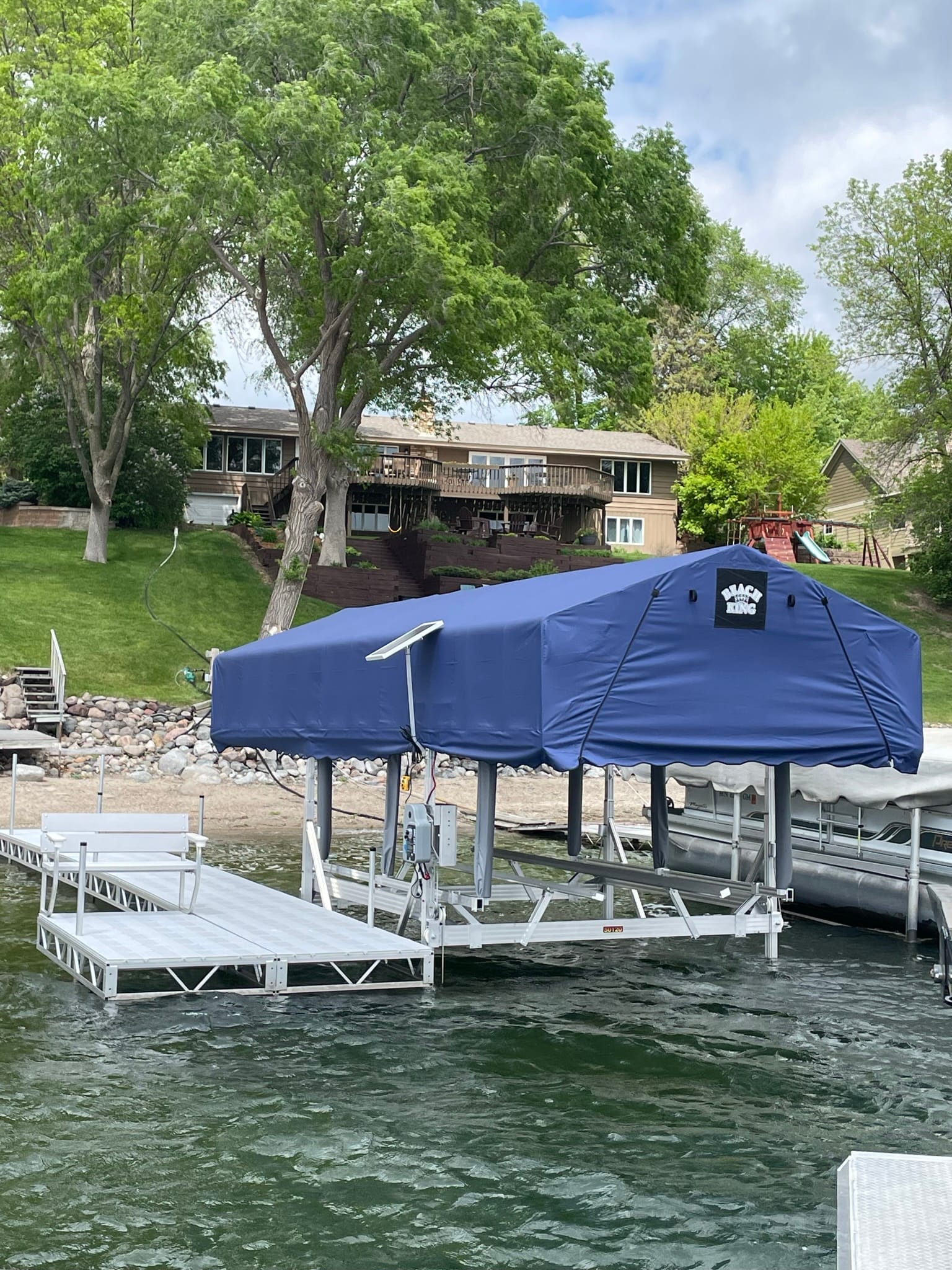 Boat lift with a blue canopy and a new white dock in front of a lake home