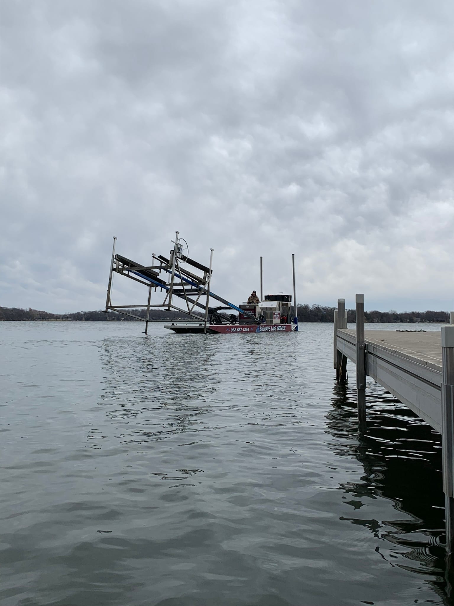 The BigWave barge carrying a boat lift frame across gray water toward a dock