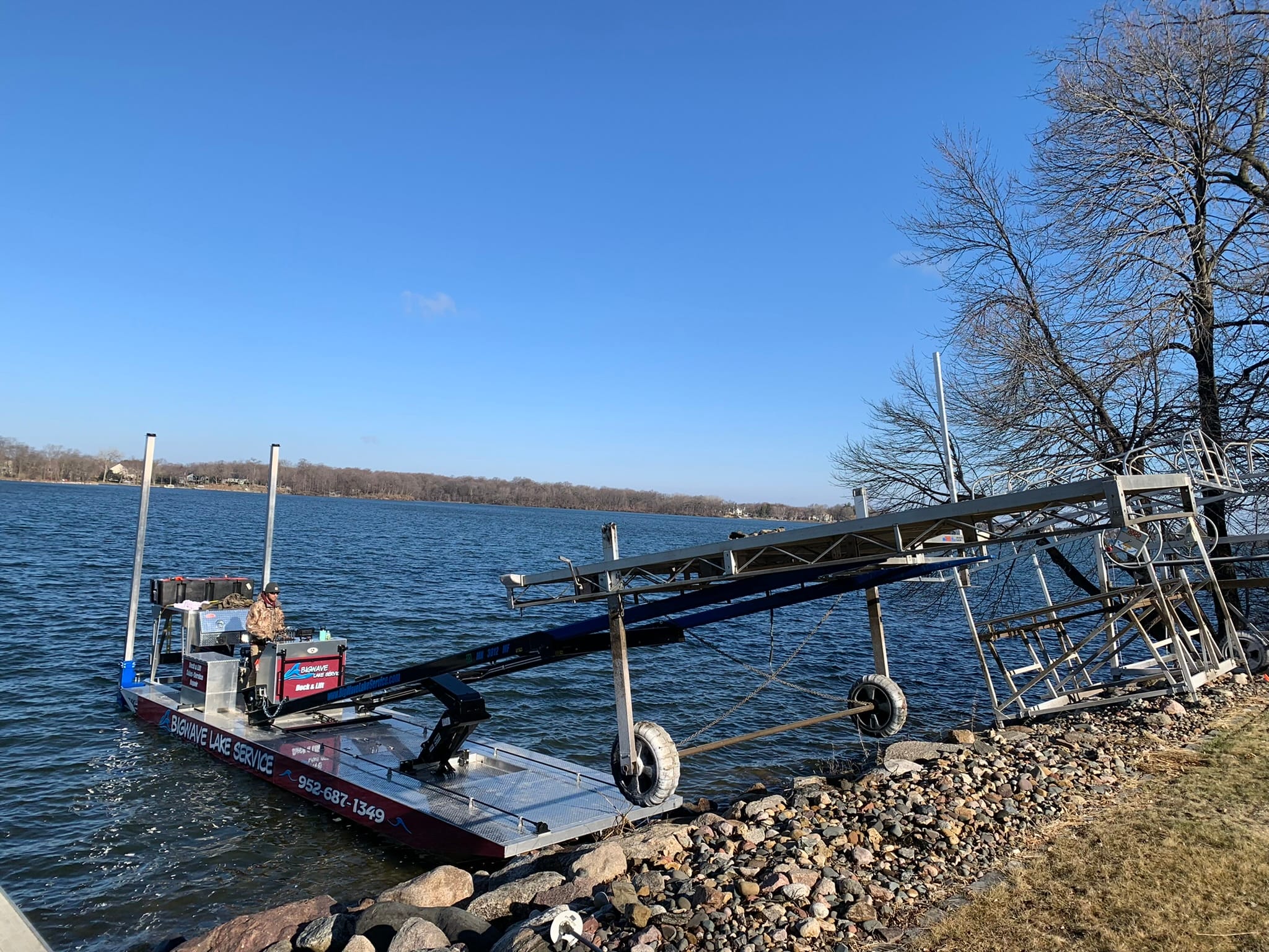 BigWave barge nosed up to a rock shoreline with its arm holding a boat lift frame over the bank