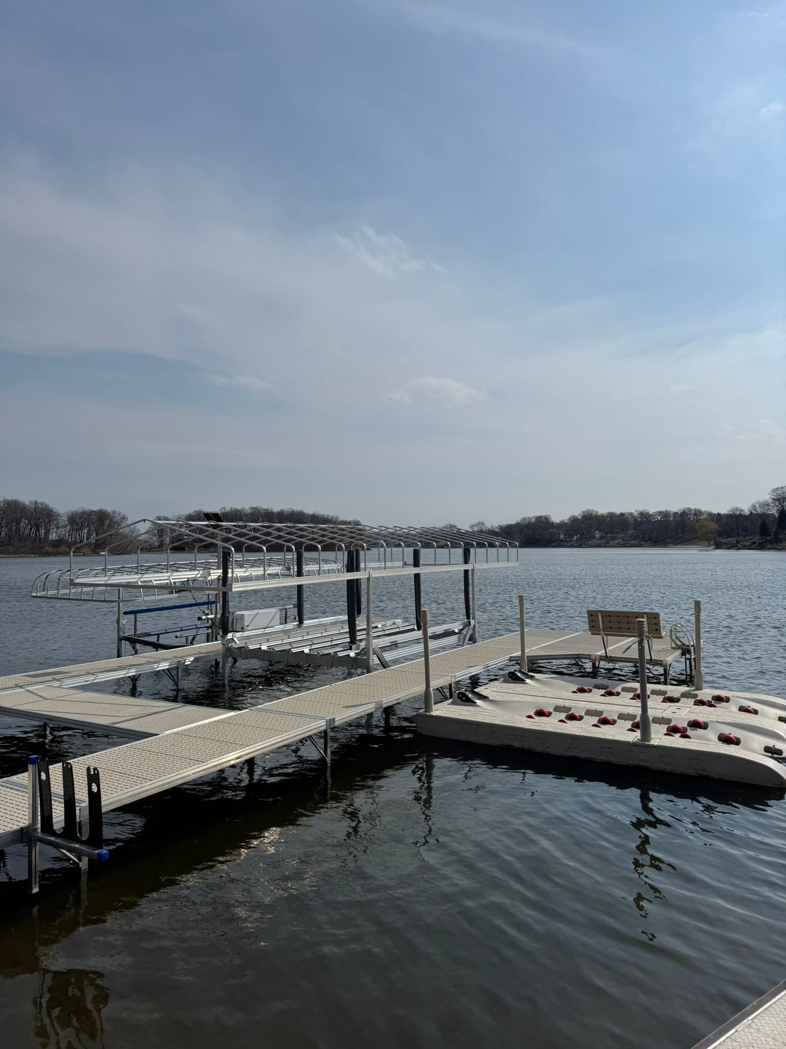 New dock with a boat lift, a bench and two drive-on jet ski ports, with bare trees across the lake