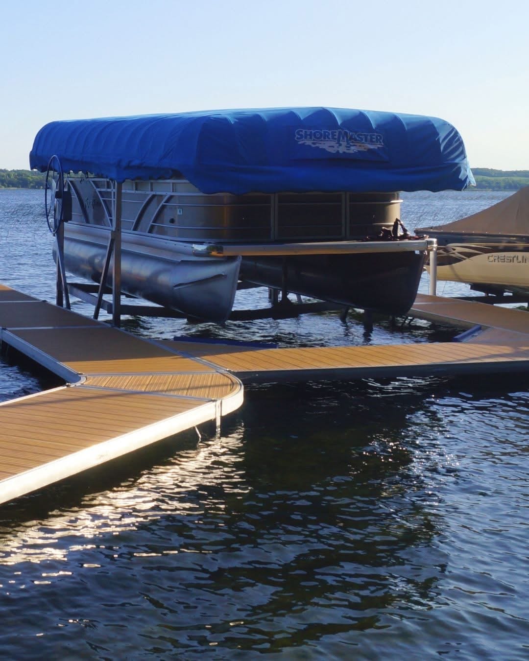 Pontoon on a canopied boat lift beside a wood-grain dock at sunset
