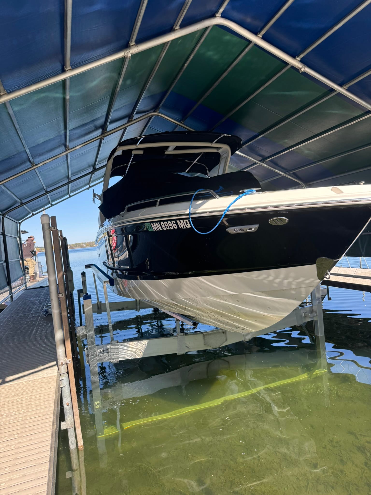 Boat sitting on a lift under a canopy, with the lift legs visible in clear green water