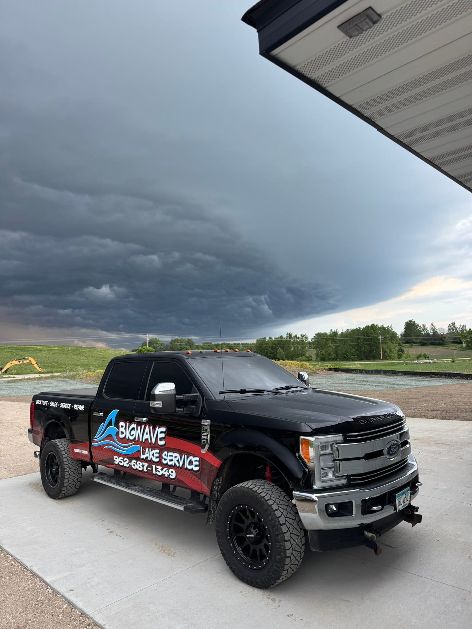 BigWave Lake Service truck parked on a concrete pad with a dark shelf cloud moving in behind it