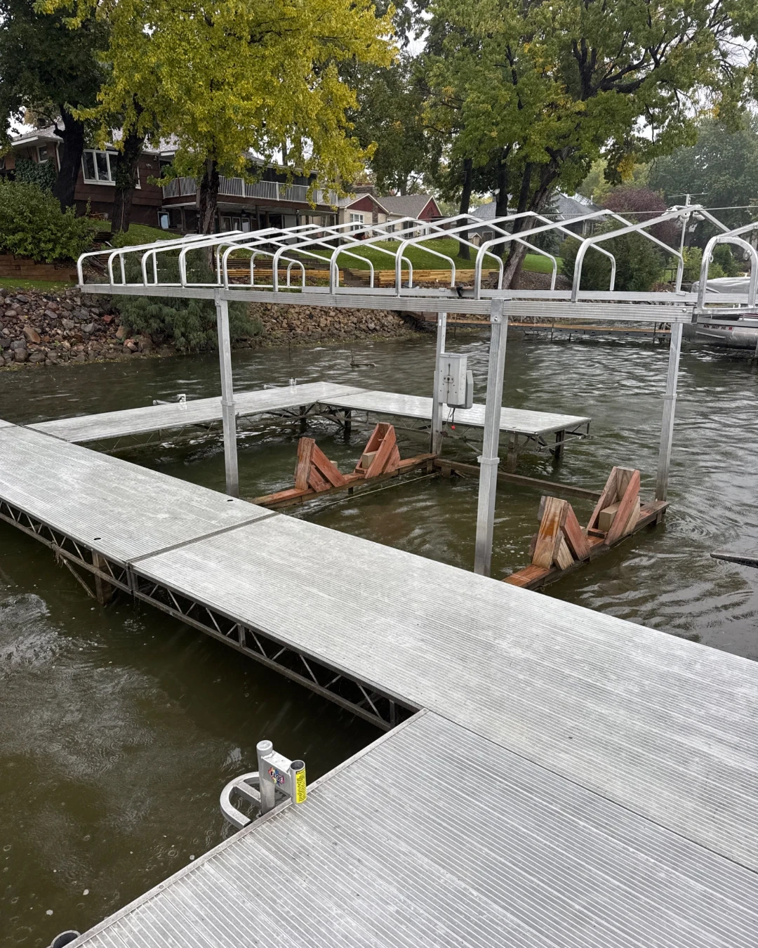 Dock and boat lift with the canopy cover off on Spring Lake, in front of a rock shoreline and lake homes in fall color