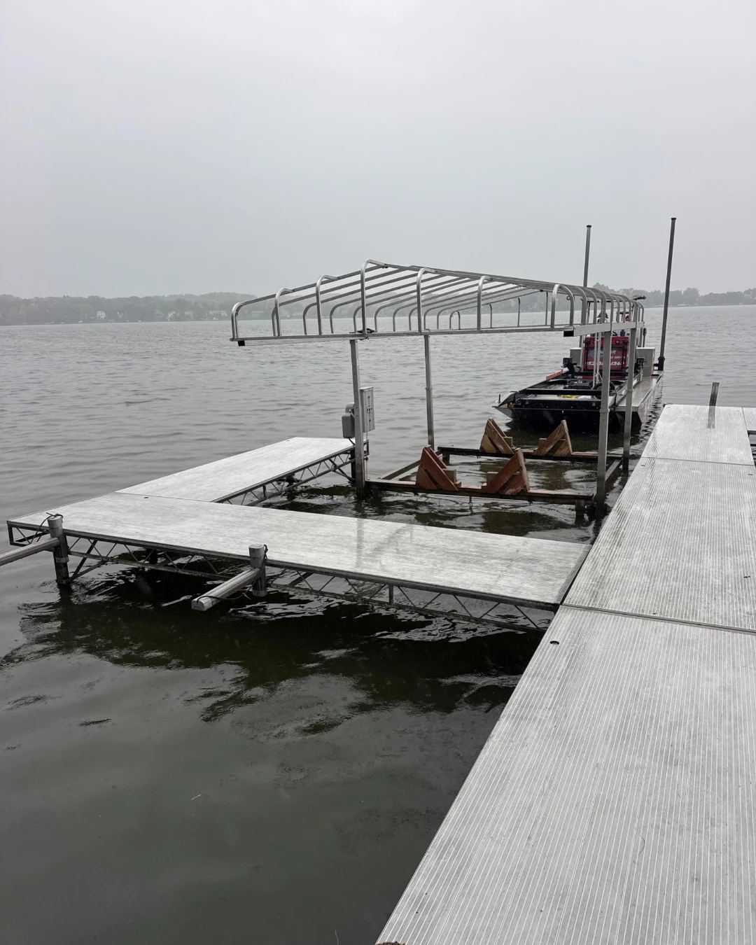 Aluminum dock and boat lift with the canopy cover off on Spring Lake, with the BigWave barge behind the lift on a gray fall day