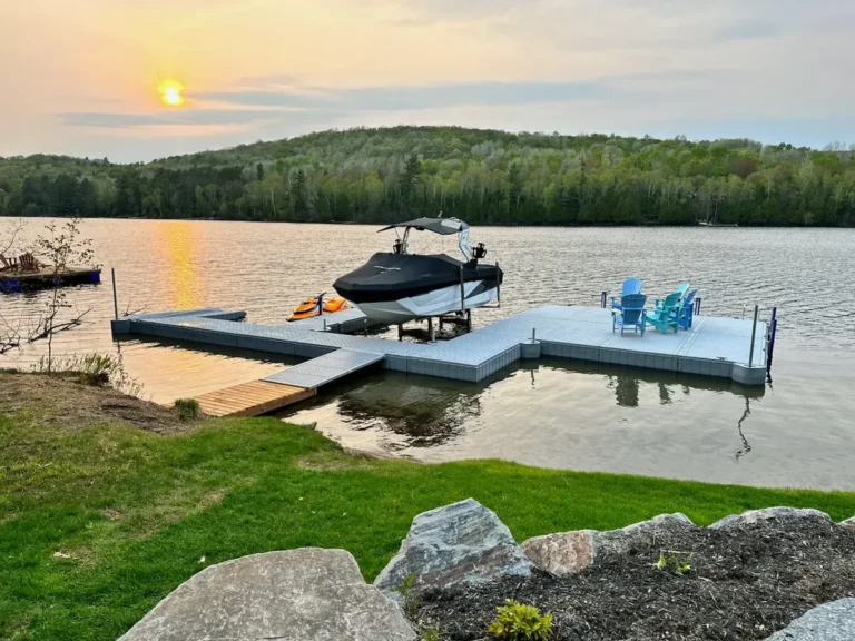 Gray floating dock on a calm lake at sunset with a wake boat tied alongside